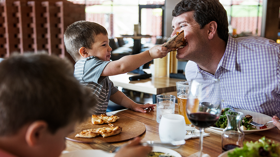 Boy feeding pizza to father in restaurant 